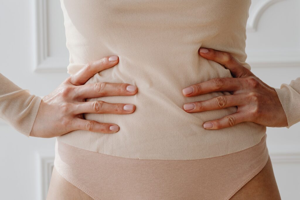 Frau stemmt beide Hände in die Hüften und zeigt ihren flachen Bauch