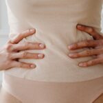 Frau stemmt beide Hände in die Hüften und zeigt ihren flachen Bauch